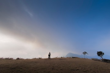 Fototapeta na wymiar Mountain view of a man standing on top hill with cloudy sky background, Phu Chi Fa (Phu Chee Fah), Chiang Rai, Thailand.