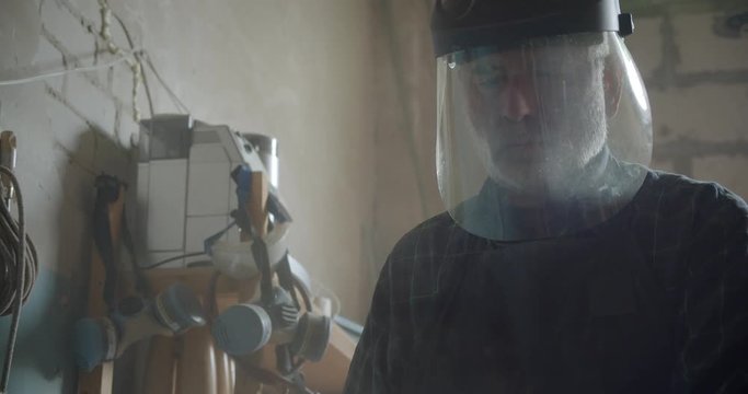 Senior male professional carpenter in safety mask working at wood manufacture being concentrated and serious.