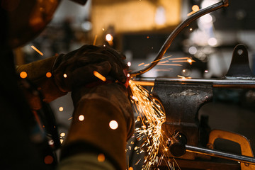 Fototapeta na wymiar Worker cutting, grinding and polishing metal part with sparks indoor workshop, close-up.