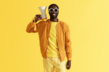 Fashion portrait of smiling black man with megaphone on yellow