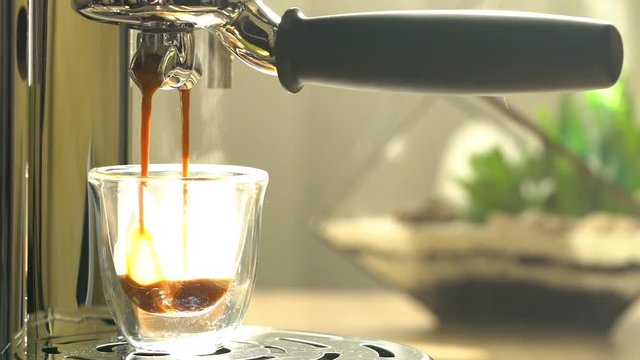 Coffee pouring into glass cup close-up, espresso machine, person taking a cup. Aromatic coffee preparation, home appliances