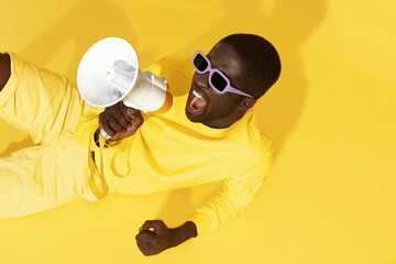Man screaming in megaphone on yellow background portrait