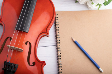 Close-up shot violin orchestra instrumental and notebook over white wooden background select focus shallow depth of field