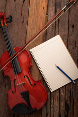 Obraz na płótnie Canvas Close-up shot violin orchestra instrumental and notebook over wooden background select focus shallow depth of field