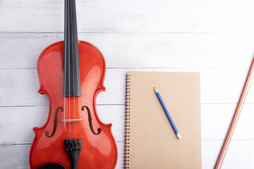 Fototapeta na wymiar Close-up shot violin orchestra instrumental and notebook over white wooden background select focus shallow depth of field