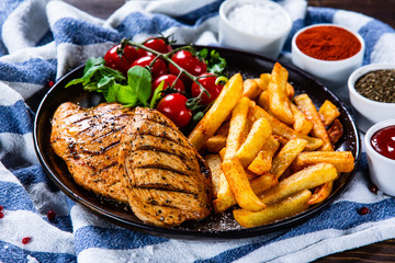 Grilled chicken fillet with french fries on wooden table