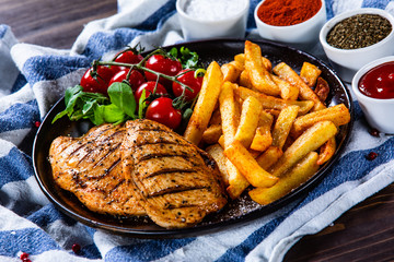Grilled chicken fillet with french fries on wooden table