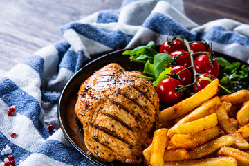 Grilled chicken fillet with french fries on wooden table