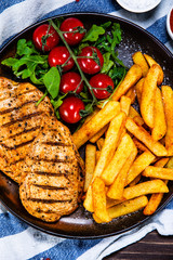 Grilled chicken fillet with french fries on wooden table