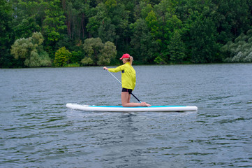 Fototapeta na wymiar Young girl paddling on SUP board on a calm lake at city. Sup surfing woman. Awesome active training in outdoor.