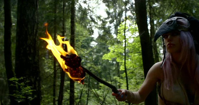 savage woman is looking around and hearing in forest in daytime, burning torch