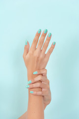 Woman hands with a turquoise color manicure in beauty studio isolated on blue soft blue background. Manicure and beauty concept. Close up, selective focus