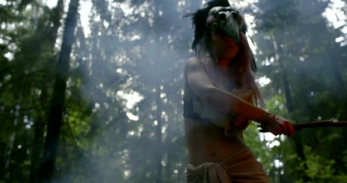 shamanic woman is performing ritual with fire in forest, wearing mask from bird skull