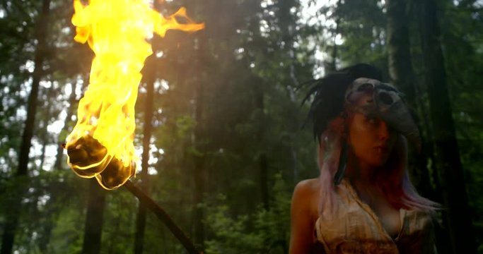 menacing female shaman is holding flaming torch in hand in forest, medium shot