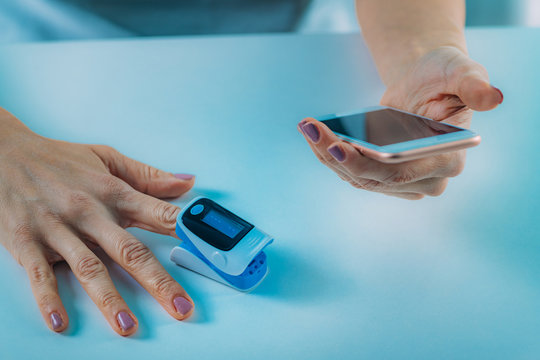 Woman Using Pulse Oximeter and Smart Phone, Measuring Oxygen Saturation
