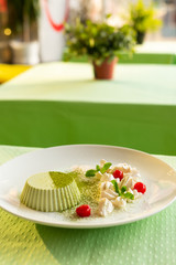 Smooth matcha panna cotta with whipped cream cheese and cherry, powdered with matcha tea and served on a green terrace