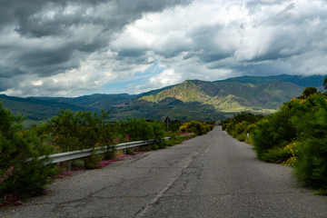 Scenic small mountain road with colorful wild flowers between villages in central part of Sicily island, Italy