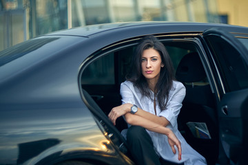 Serious woman sitting in the car over modern office facade