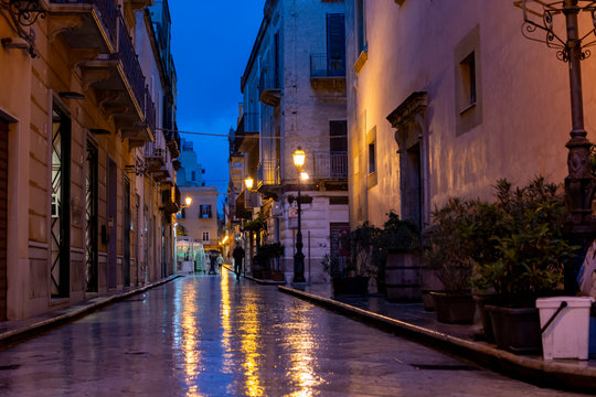 Fototapeta Old street in Marsala at night in rain with reflection of street lights on water, Sicily, Italy