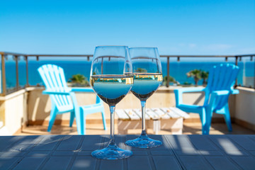 Two wine glasses with white wine served on outdoor terrace witn blue sea and mountains view on background