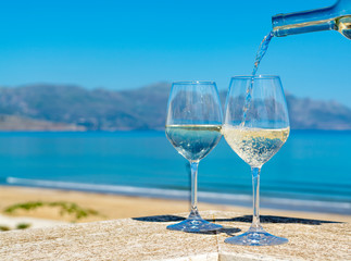 Waiter pouring white wine in wine glasses on outdoor terrace witn blue sea and mountains view on background