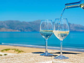 Waiter pouring white wine in wine glasses on outdoor terrace witn blue sea and mountains view on...