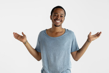 Beautiful male portrait on white studio background. Young emotional african-american man in blue shirt. Facial expression, human emotions, ad concept. Smiling, inviting, showing empty space bar.