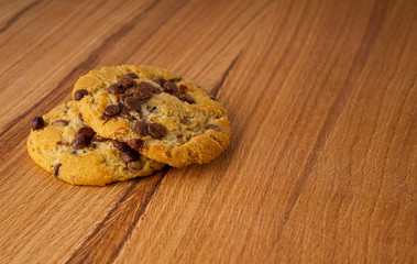 Two homemade cookies with chocolate pieces on a light wood table