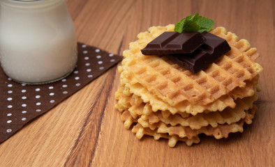 Crispy Belgian waffles with chocolate chips. A small glass cup with milk on a brown polka dot napkin