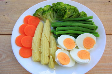 Fresh green broccoli,carrot,Lentils,Baby corn,and egg in white disc on the wood table, healthy or vegetarian food concept Top view.