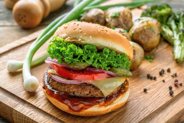 Cheeseburger made of meat burger, cheese, tomato, lettuce, onion and pickled cucumber with baked potato and broccoli.