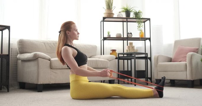 Woman in sportswear doing seated row exercises with resistance band at home