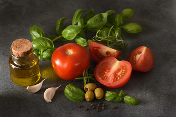 The ingredients for the salad with the tomatoes and olive oil on the dark background. The sliced ​​tomatoes