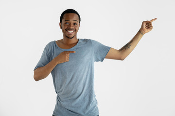 Beautiful male portrait isolated on white studio background. Young emotional african-american man in blue shirt. Facial expression, human emotions, ad concept. Smiling, inviting, pointing up.