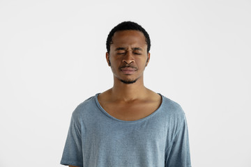 Beautiful male half-length portrait isolated on white studio background. Young emotional african-american man in blue shirt. Facial expression, human emotions, ad concept. Thinking with closed eyes.