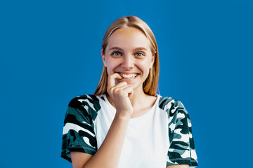 Blonde woman over blue studio background interested of something, flirt and like someone, feel fun and joy, ready to surprise