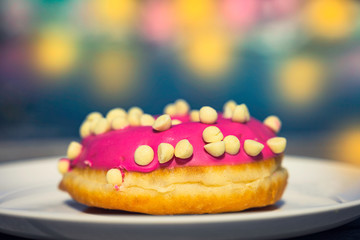 Delicious donut with pink creams decorated with white chocolate on white plate with colourful background