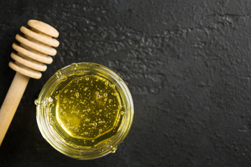 Homemade spa with flower honey in glass jar with wooden stick over black stone background with copy space