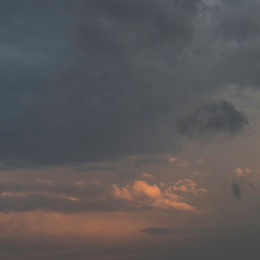 Cloudscape with thunderstorm clouds and some orange shining light through the sky. In the Clouds there is copy space.