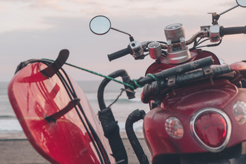 Moto con tabla de surf aparcada frente al mar al atardecer 