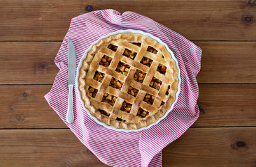 food, culinary and eating concept - close up of apple pie in baking mold with knife on kitchen towel