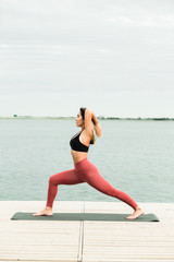 Asian young girl doing yoga outdoors on the pier by the lake.