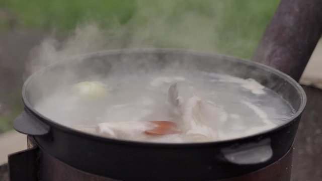 Cooking fish soup outdoors, on the surface of the water foam and plentiful steam, close-up shot, summer