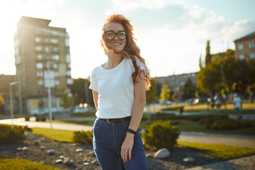 Portraits of a charming red-haired girl with a cute face. Girl posing for the camera in the city...