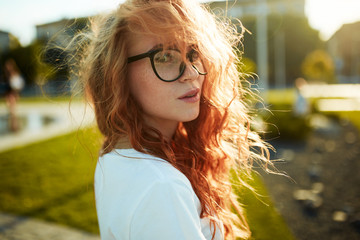 Portraits of a charming red-haired girl with a cute face. Girl posing for the camera in the city...