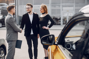 Obraz premium Couple in a car salon. Family buying the car. Elegant woman with her husband. Assistant with a clients