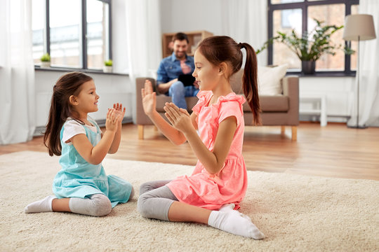 childhood, leisure and family concept - happy little sisters playing clapping game at home
