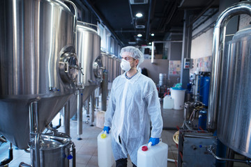 Technologist industrial worker holding plastic canisters about to change chemicals in the food...