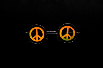Vintage sunglasses with a symbol of pacifist motion on a black surface.