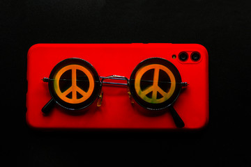 Vintage sunglasses with the symbol of pacifist movement lie on the red phone.